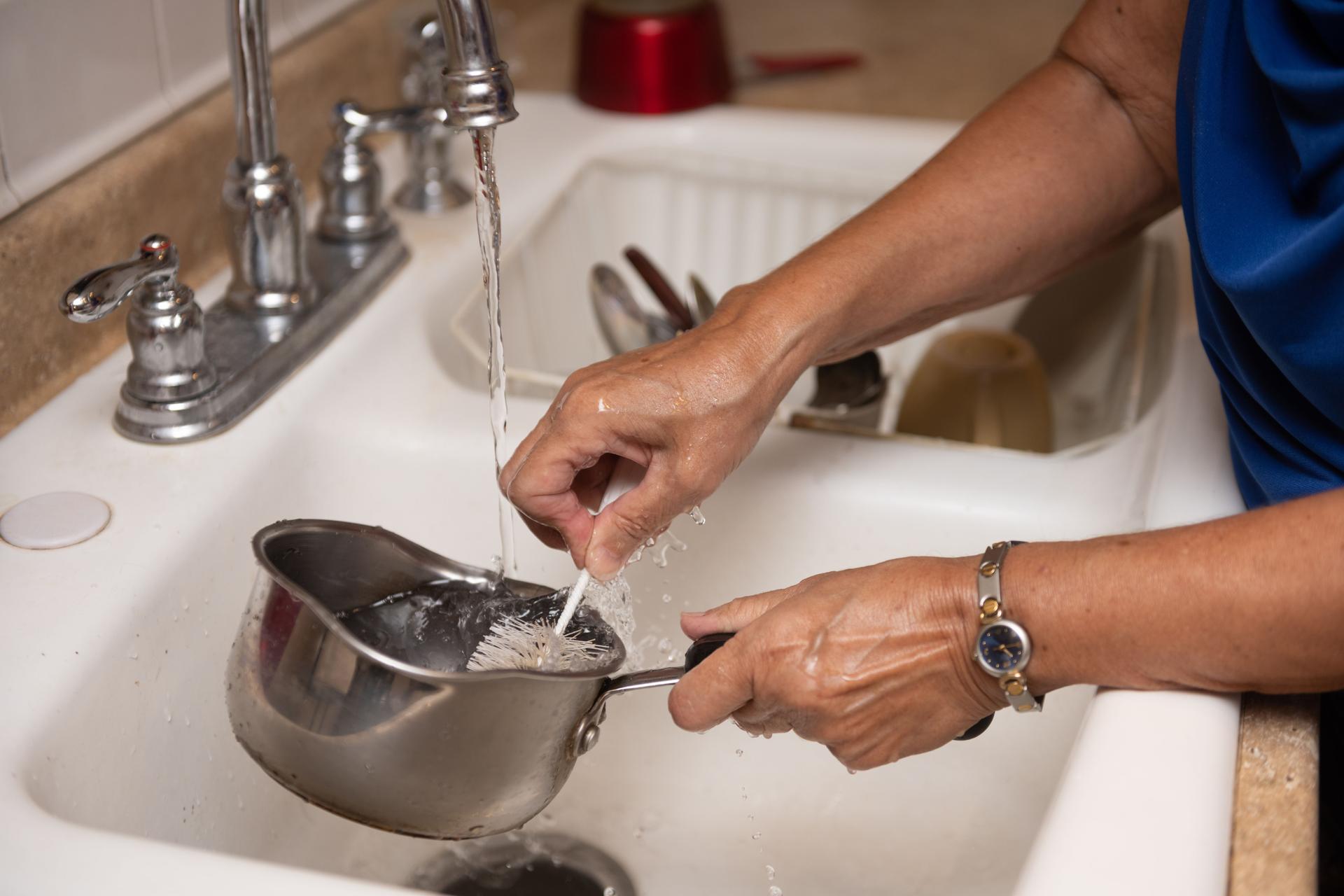 Hands of Senior Hispanic Woman Washing Dishes in the Kitchen Sink